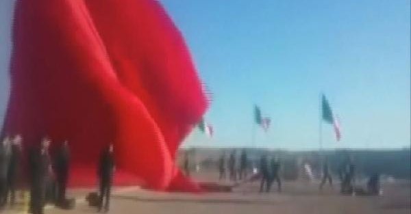 Dev bayrağı tutmaya çalışan asker rüzgarla birlikte havaya savruldu